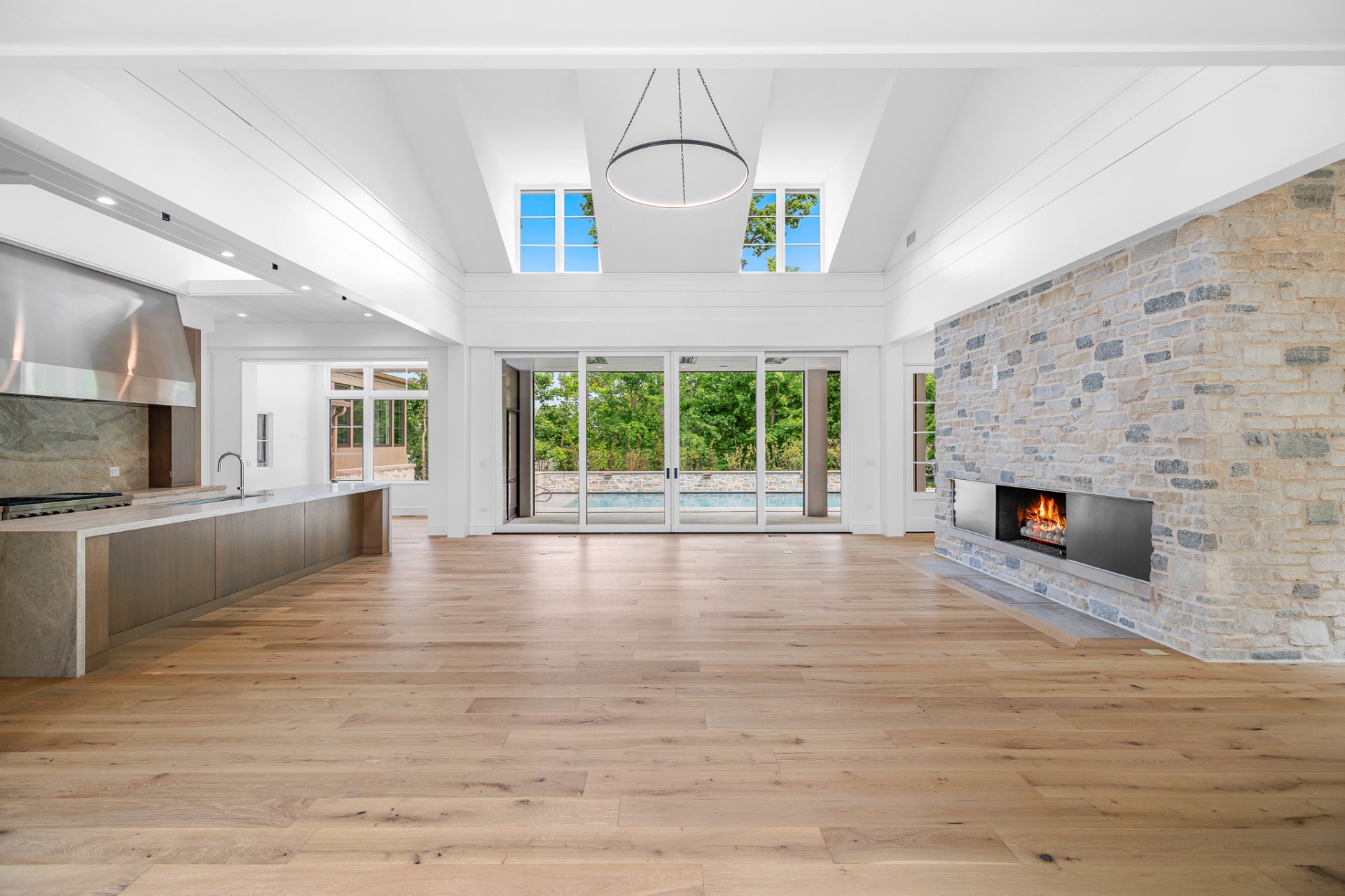 Great room with vaulted ceiling, stone fireplace, and pool view